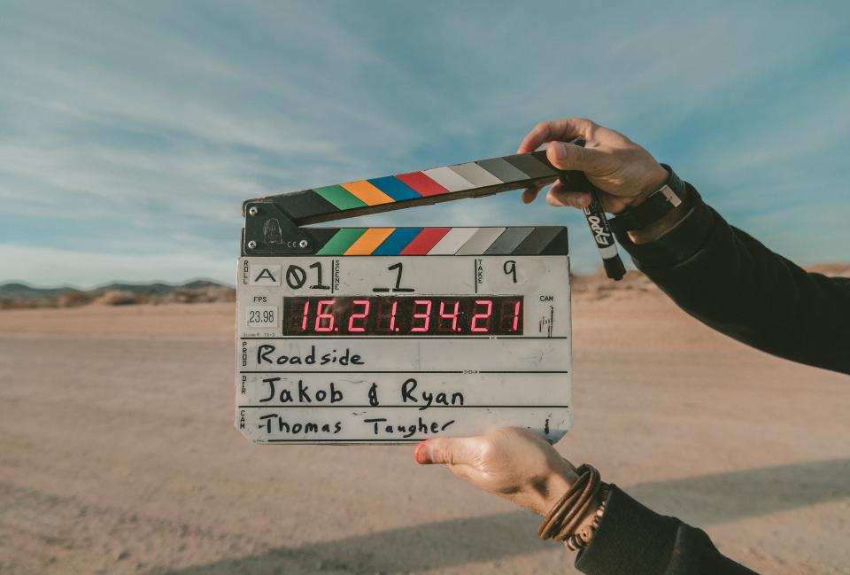 Claquete de filmagem sendo aberta por duas mãos, com deserto e céu ao fundo