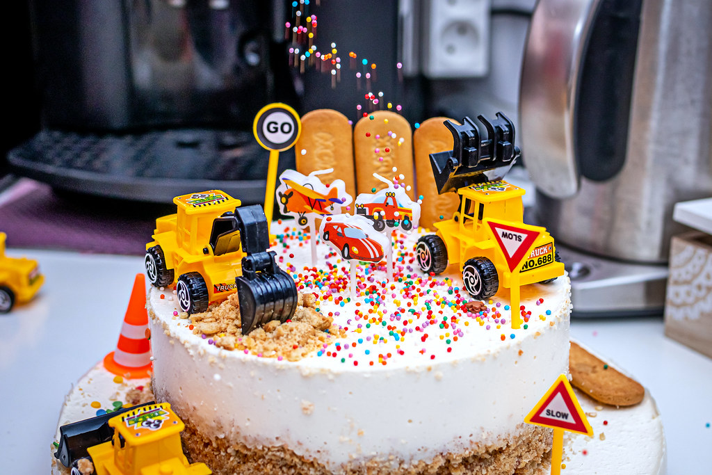 Bolo de festa infantil decorado com caminhões de brinquedo e confeitos coloridos