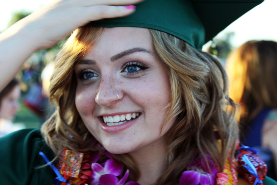 Retrato de uma formanda sorridente, usando capelo verde e colares de formatura