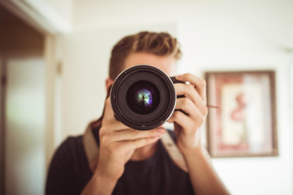 Fotógrafo apontando uma câmera profissional diretamente para a lente, em ambiente interno