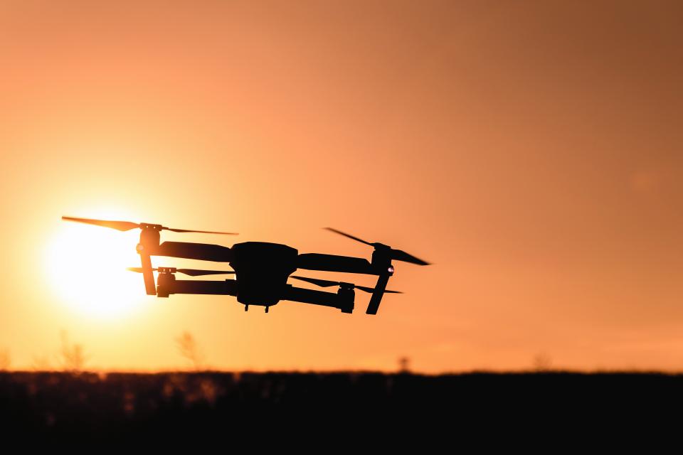 Silhueta de um drone voando contra o sol se pondo no horizonte