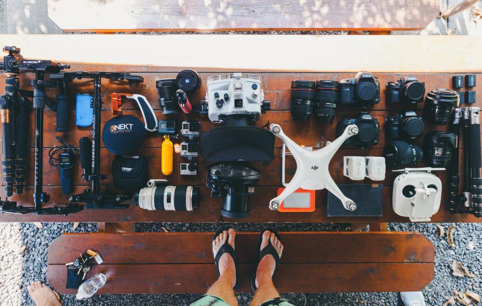 Equipamento de filmagem organizado sobre uma mesa de madeira: câmeras, lentes, drone, baterias e acessórios