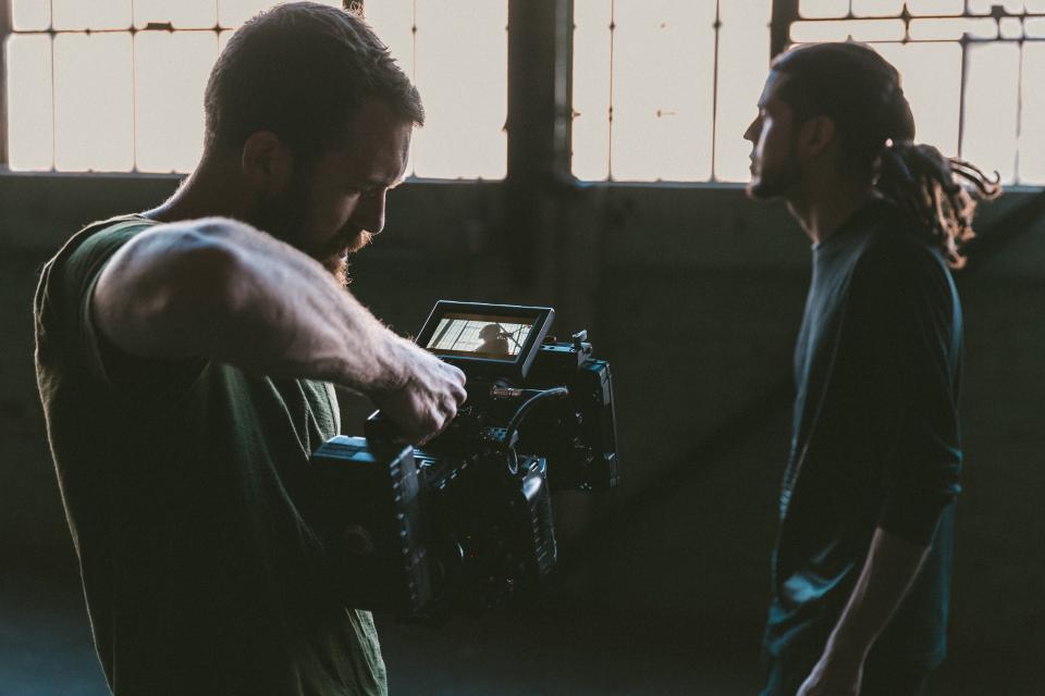 Videomaker operando uma câmera de cinema no ombro durante uma gravação num galpão
