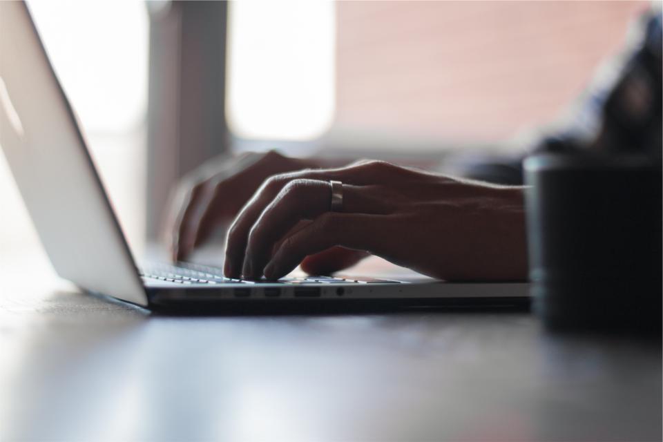 Mãos digitando em um notebook sobre uma mesa de madeira