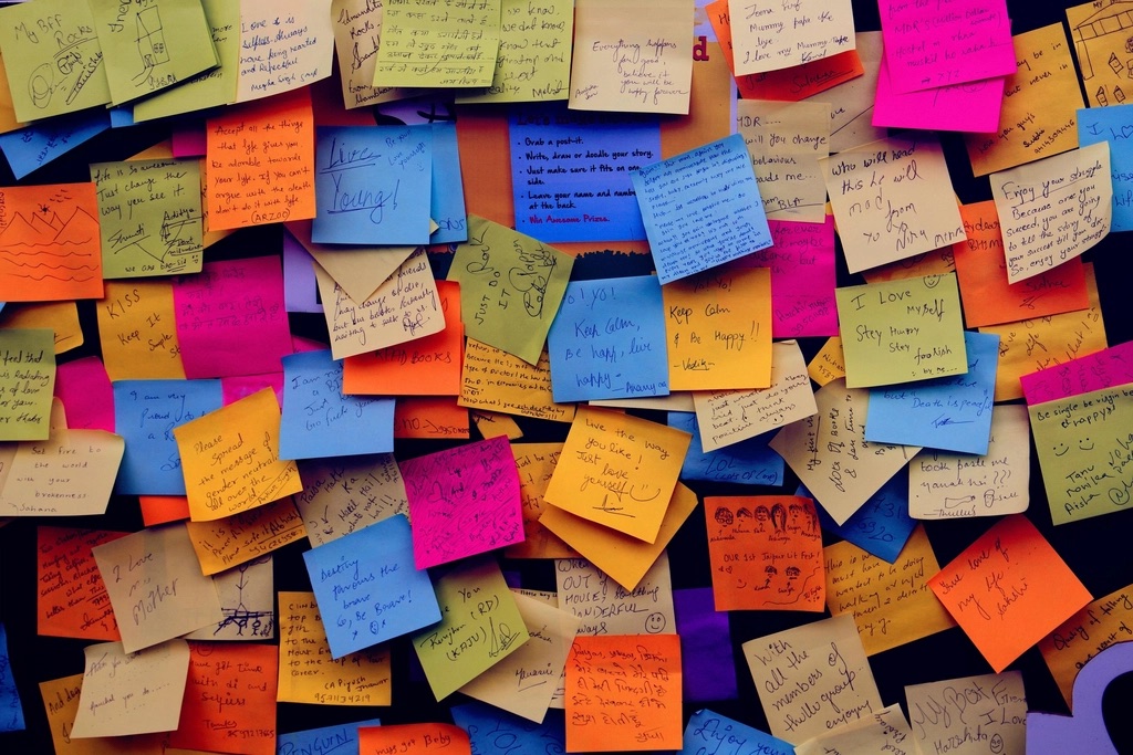 Parede inteira coberta de post-its coloridos escritos à mão, uns sobre os outros
